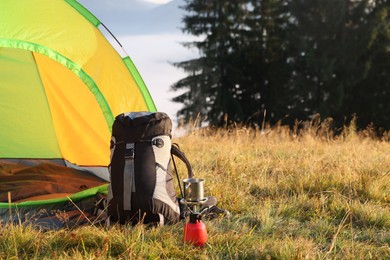 Camping tent, backpack and burner with metal mug outdoors. Space for text