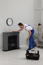 Professional technician using construction level for installing electric fireplace in room