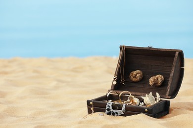 Open wooden chest with treasures on sandy beach, space for text