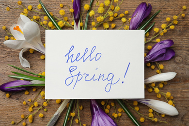 Card with words HELLO SPRING and fresh flowers on wooden table, flat lay