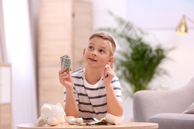 Little boy with broken piggy bank and money at home