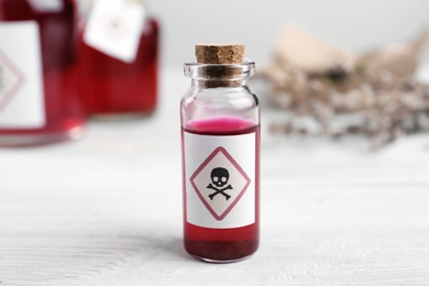 Vial of poison with warning sign on white wooden table, closeup