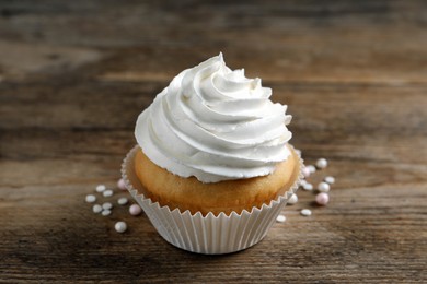 Delicious cupcake with cream on wooden table, closeup