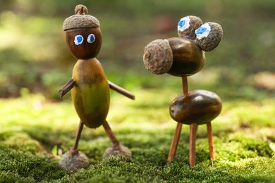 Photo of Cute figures made of acorns on green moss outdoors, closeup