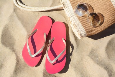 Pink flip flops, sunglasses and straw bag on sand, flat lay. Beach accessories