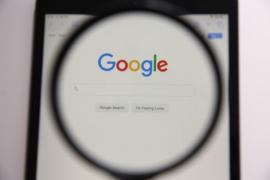 MYKOLAIV, UKRAINE - OCTOBER 30, 2020: Looking through magnifying glass at screen with Google search bar on white background