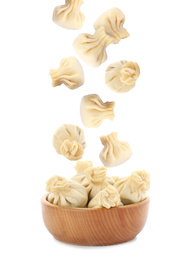Many tasty dumplings falling into wooden bowl on white background