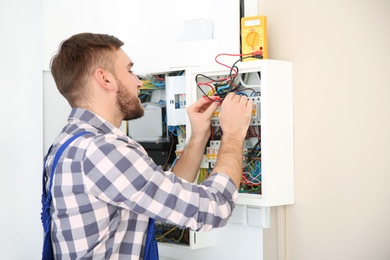 Photo of Electrician with digital multimeter checking voltage indoors