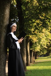 Young nun reading Bible in park on sunny day. Space for text
