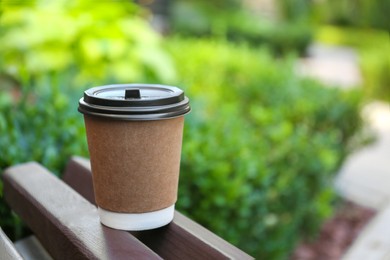 Disposable paper cup with plastic lid on wooden bench outdoors, space for text