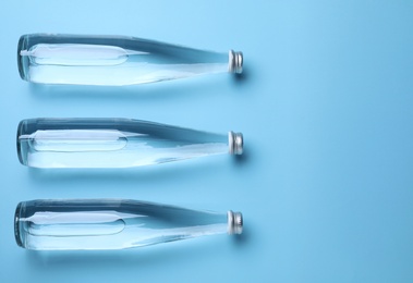 Glass bottles with water on light blue background, flat lay. Space for text