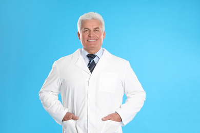 Happy senior man in lab coat on light blue background