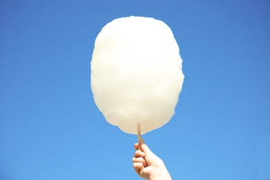 Woman holding white cotton candy against blue sky