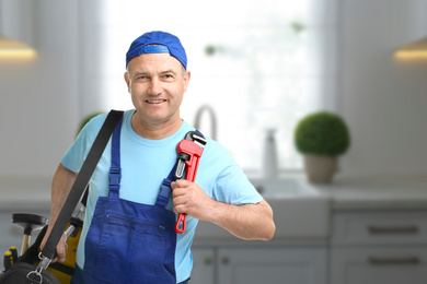 Mature plumber with pipe wrench and tool bag in kitchen, space for text