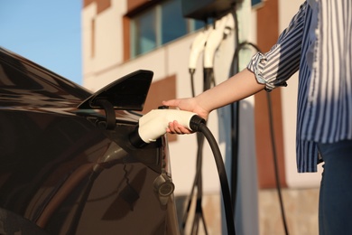 Woman inserting plug into electric car socket at charging station, closeup