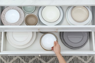Photo of Woman taking ceramic bowl from open drawer in kitchen, top view