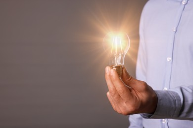 Glow up your ideas. Closeup view of man holding light bulb on grey background, space for text