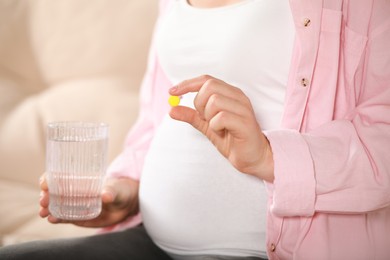Pregnant woman holding pill and glass with water on blurred background, closeup