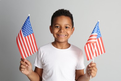 Happy African-American boy holding national flags on light grey background