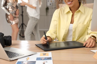 Professional retoucher working with graphic tablet at desk in photo studio, closeup