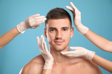 Doctors examining man's face for cosmetic surgery on light blue background