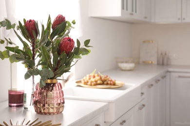 Photo of Beautiful protea flowers on countertop in kitchen, space for text. Interior design