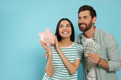 Happy couple with money and ceramic piggy bank on light blue background, space for text