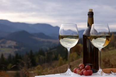 Photo of Tasty wine and fresh grapes on white wooden table against mountain landscape. Space for text