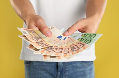 Man with Euro banknotes on yellow background, closeup