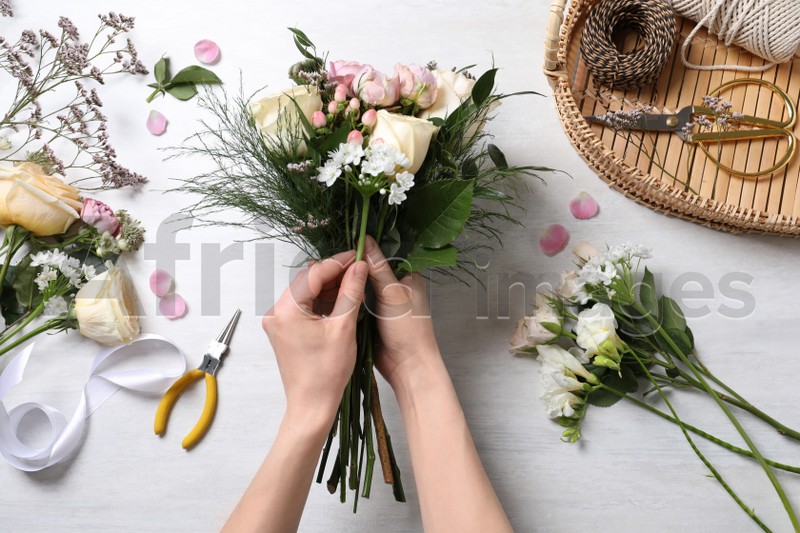Florist making beautiful bouquet with roses at white table, top view