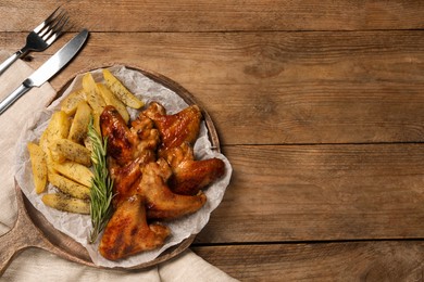 Board with delicious fried chicken wings and potatoes on wooden table, top view. Space for text