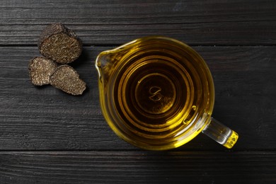 Photo of Fresh truffle oil in glass jug on black wooden table, flat lay