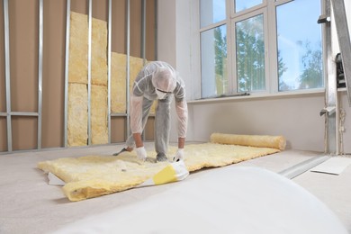 Worker measuring and cutting insulation material indoors