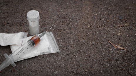 Photo of Plastic bags, container with powder and syringe on asphalt, space for text. Hard drugs
