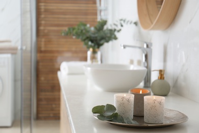 Tray with eucalyptus leaves and burning candles on countertop in bathroom