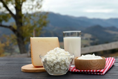 Tasty cottage cheese and other fresh dairy products on black wooden table in mountains
