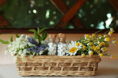 Bottles with homeopathic remedy and flowers in basket on wooden table