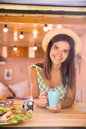 Young woman with cup in trailer, view from outside. Camping vacation