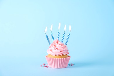 Delicious birthday cupcake with burning candles and sprinkles on light blue background