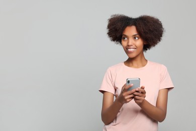 Photo of Smiling African American woman with smartphone on light grey background. Space for text