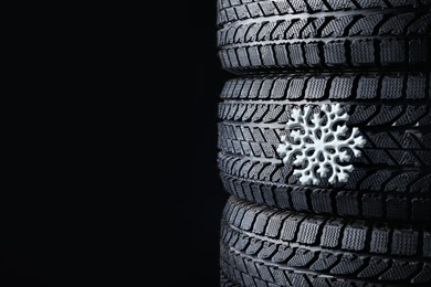 Stacked winter tires with snowflake on black background, closeup. Space for text