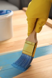 Worker applying blue paint onto wooden surface, closeup