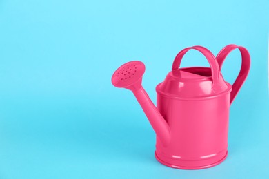 Photo of Pink metal watering can on light blue background, space for text