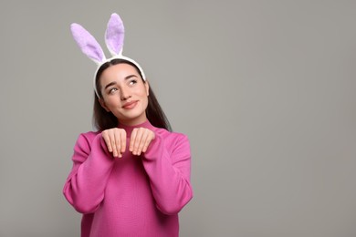 Photo of Happy woman wearing bunny ears headband on grey background, space for text. Easter celebration