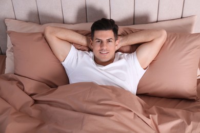 Man lying in comfortable bed with beige linens, above view