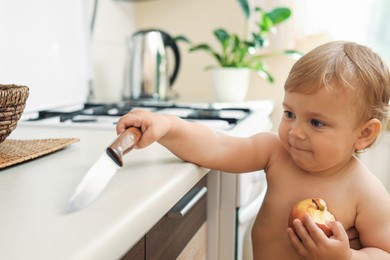 Photo of Little child holding sharp knife in kitchen. Dangerous situation