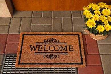 Door mat with word Welcome and beautiful flowers near entrance