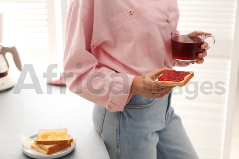 Woman having tasty breakfast with toast and raspberry tea at home, closeup. Morning routine