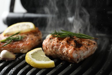 Tasty salmon cooking with rosemary and lemon slice on electric grill, closeup