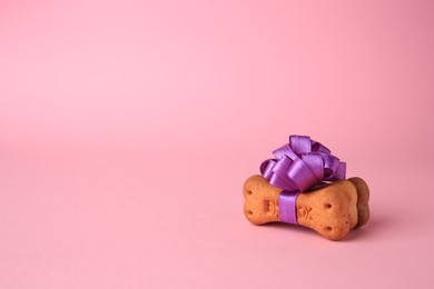 Photo of Bone shaped dog cookies with purple bow on pink background. Space for text